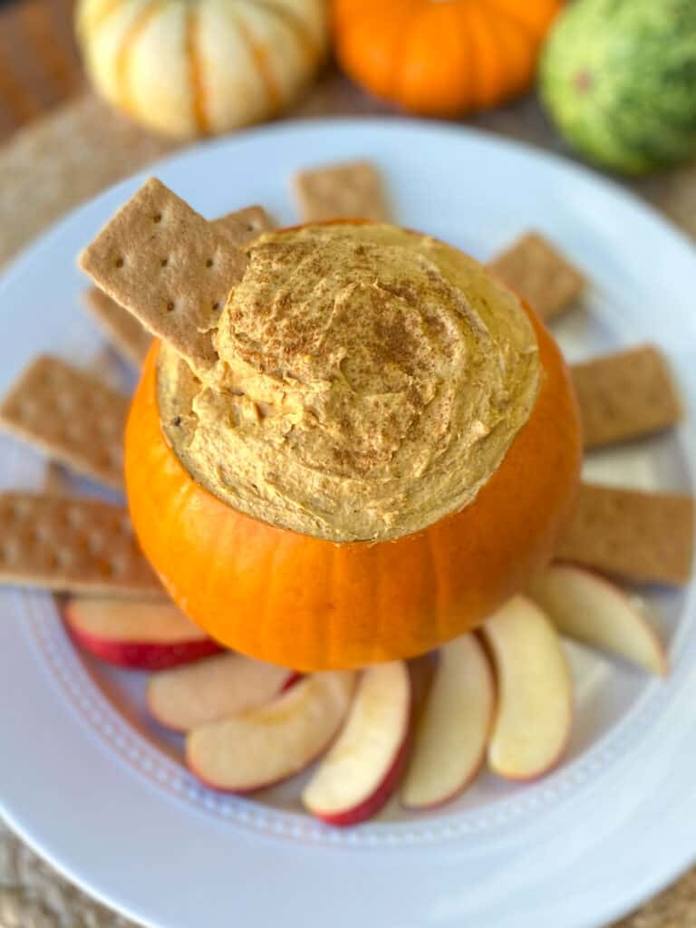 close up of pumpkin dip in a carved out pumpkin with graham crackers and apples slices on a plate