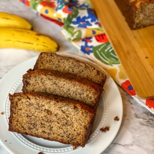 banana bread slices a plate with a loaf and bananas in the background
