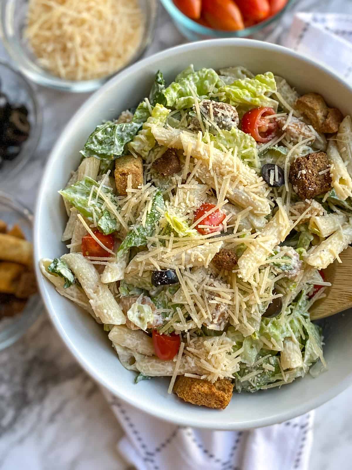 Caesar Pasta Salad in a bowl with ingredients in small bowls in the background