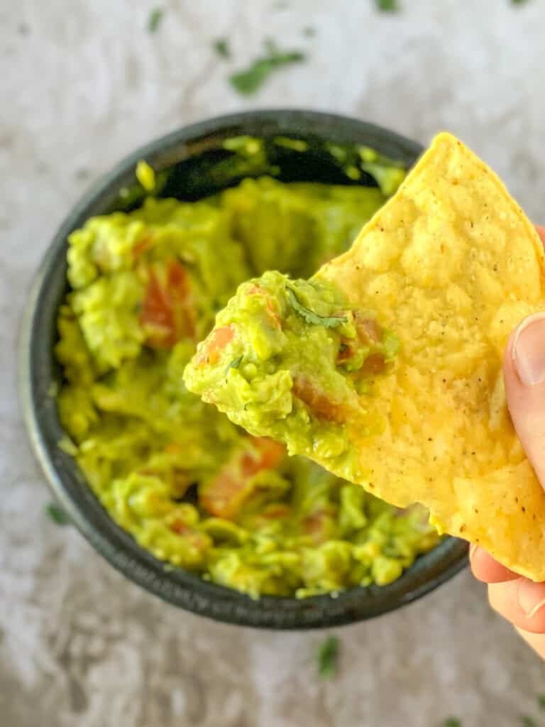 close up of guacamole on a chip with a bowl of guacamole in the background