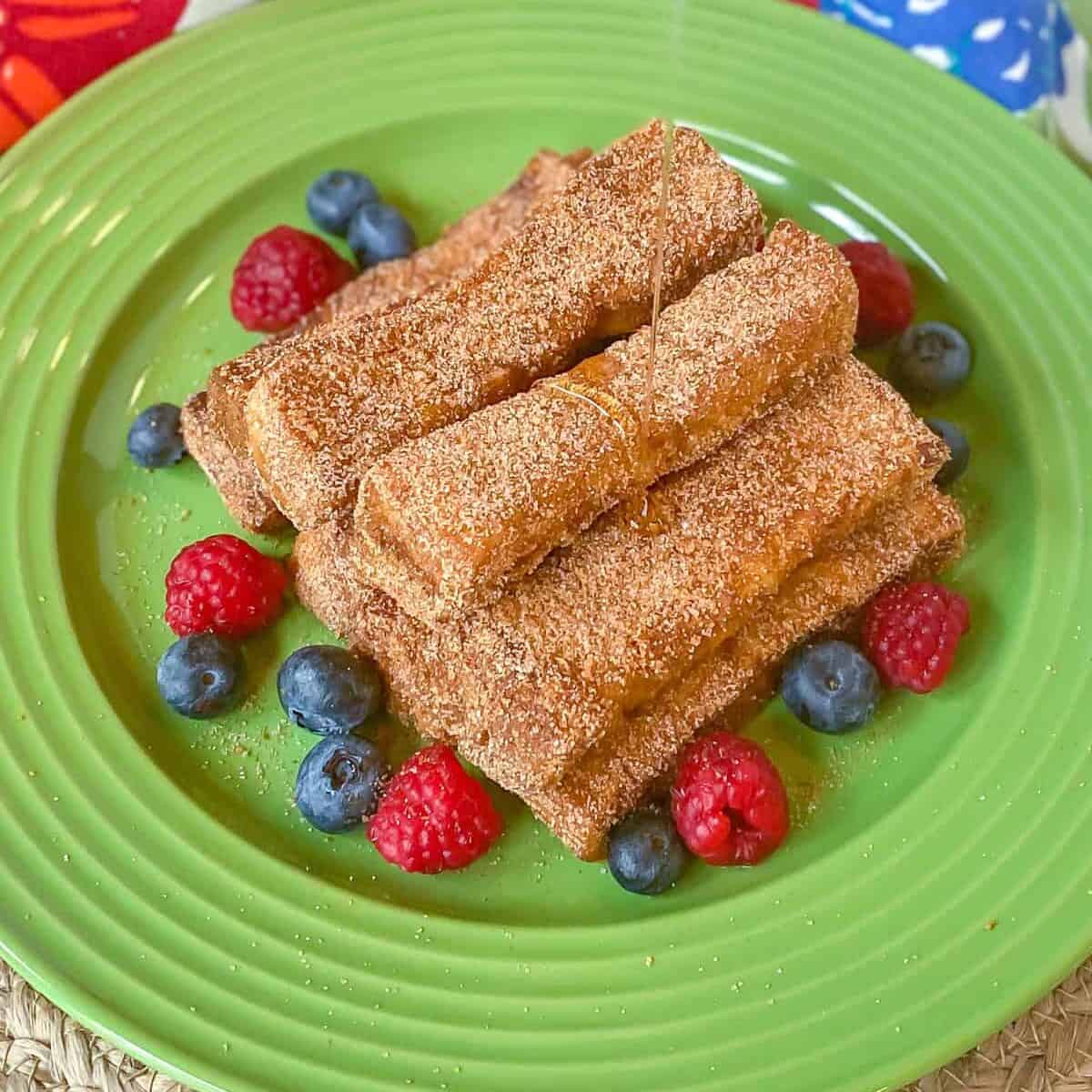 cinnamon french toast sticks on plate with berries and syrup