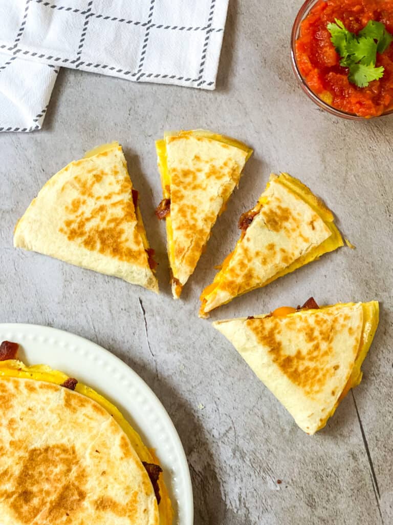 breakfast quesadillas cut into 4 pieces, on a plate, and salsa in a cup