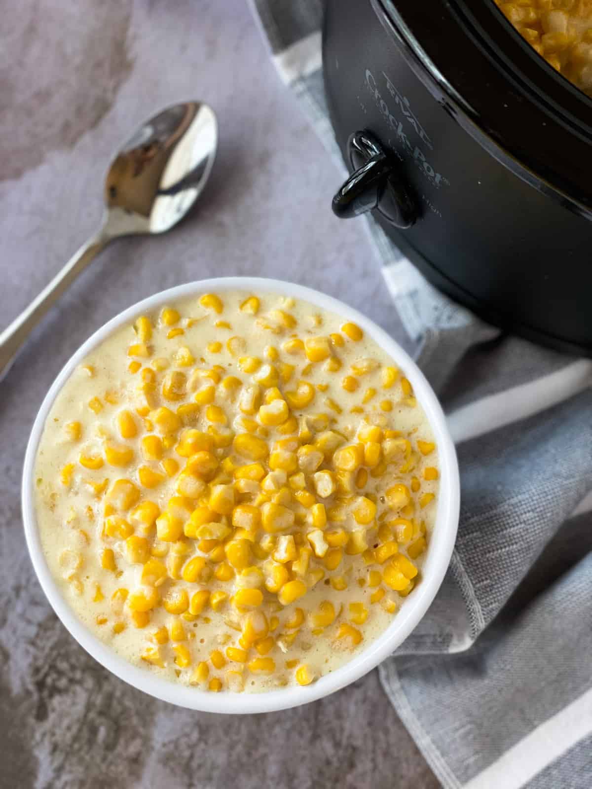 bowl of creamed corn, spoon, and crockpot