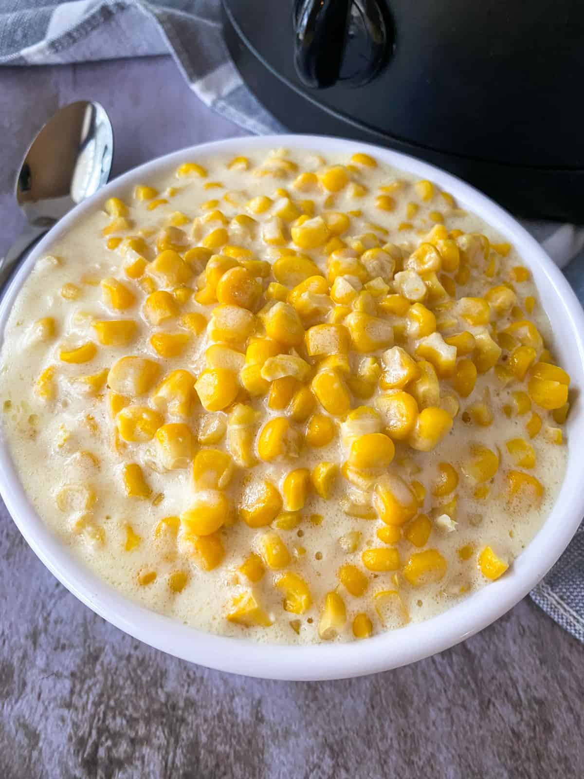 bowl of 5 ingredient slow cooker creamed corn with a spoon and crockpot in the background