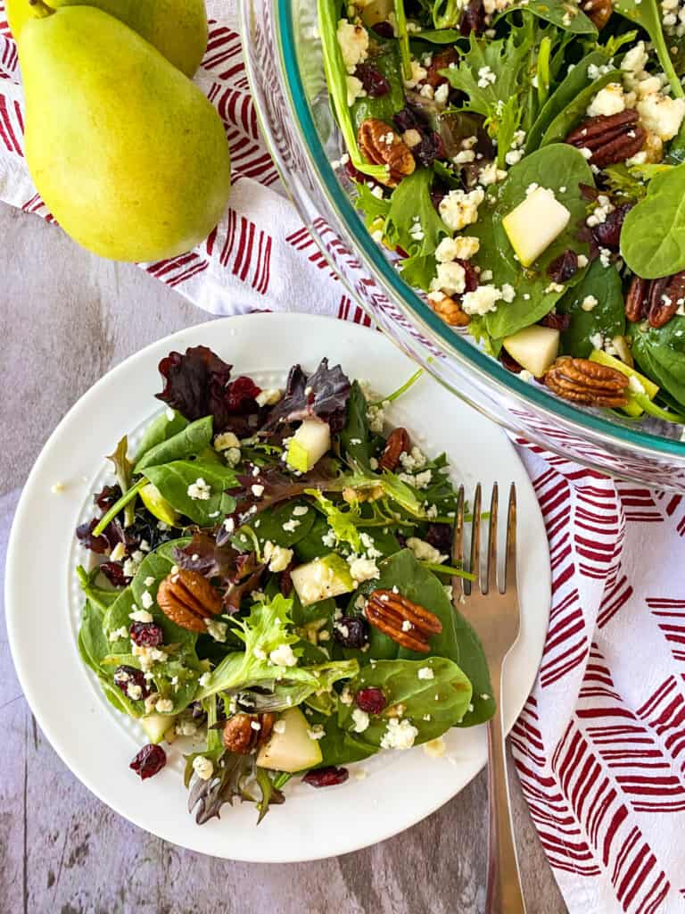 candied pecan and cranberry pear salad on a plate, in a bowl, with a pear on the side