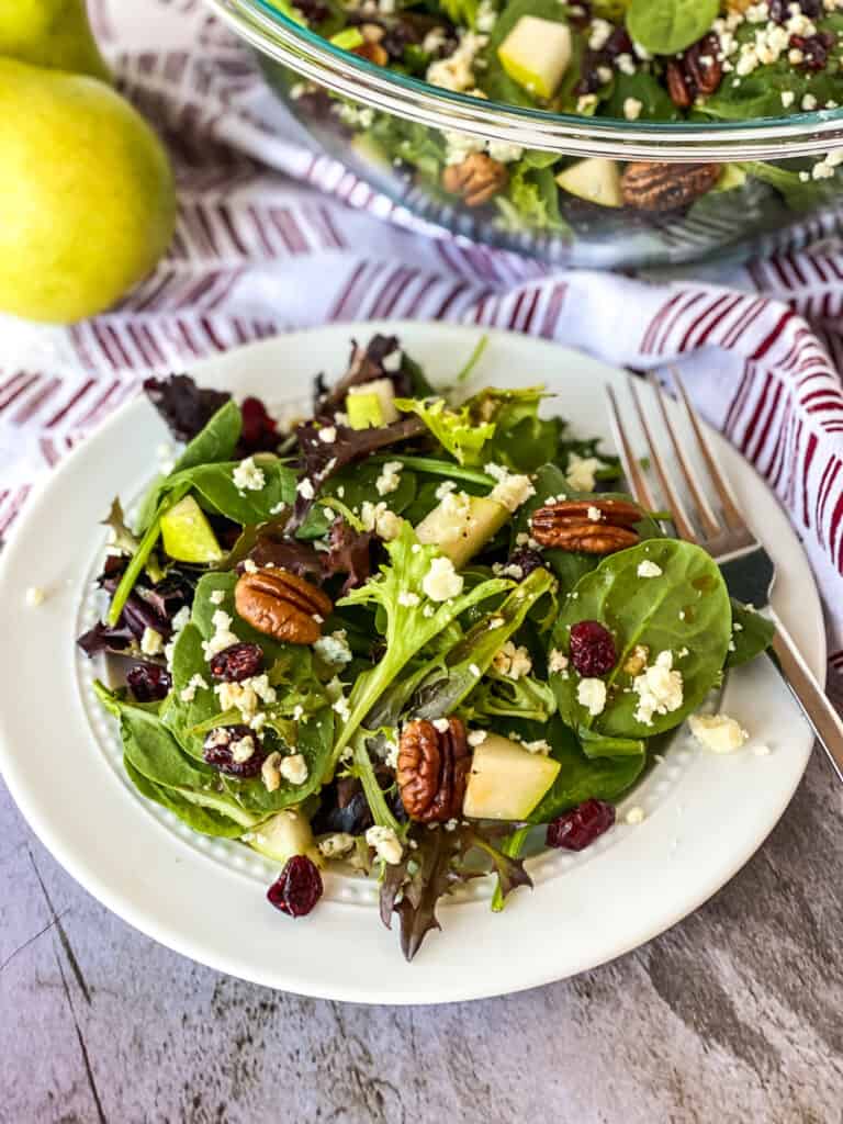 candied pecan and cranberry pear salad on a plate, in a bowl, and a pear to the side
