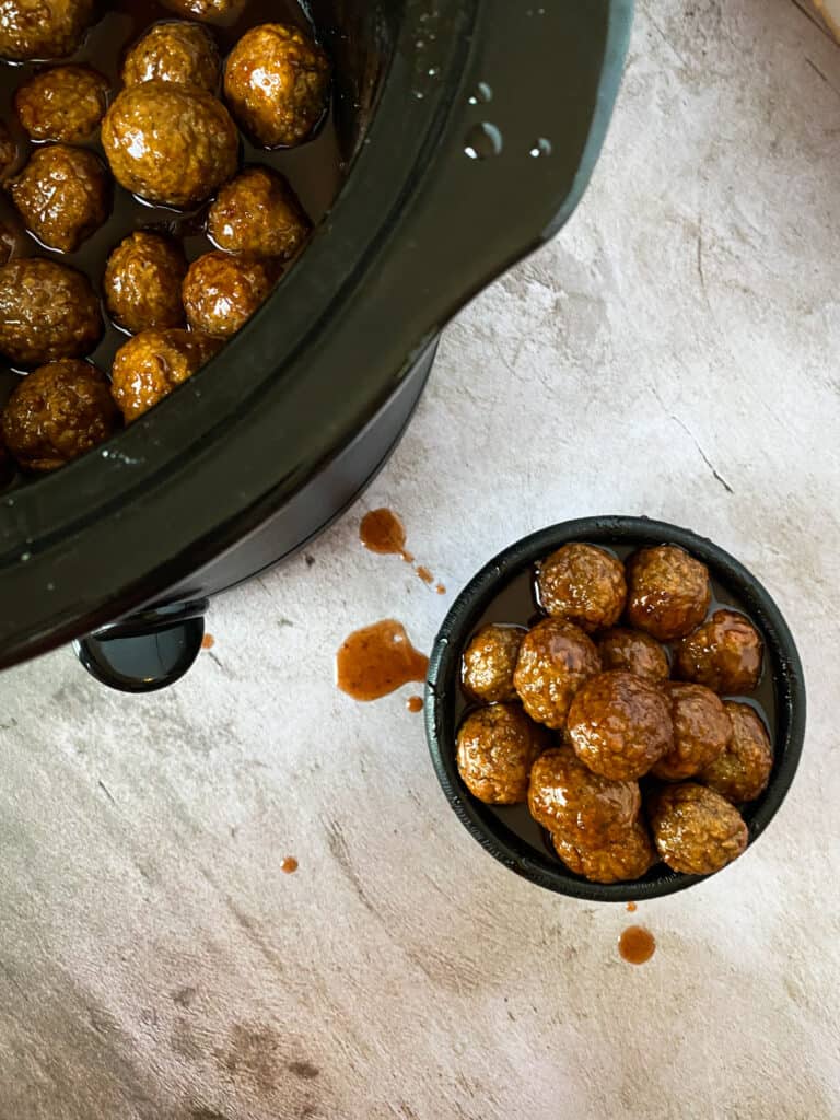 bowl and crockpot full of slow cooker bbq grape jelly meatballs