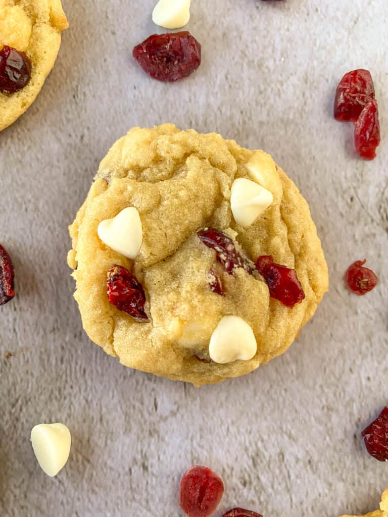 close up of white chocolate chip cranberry sugar cookie with cranberries and white chocolate chips scattered around