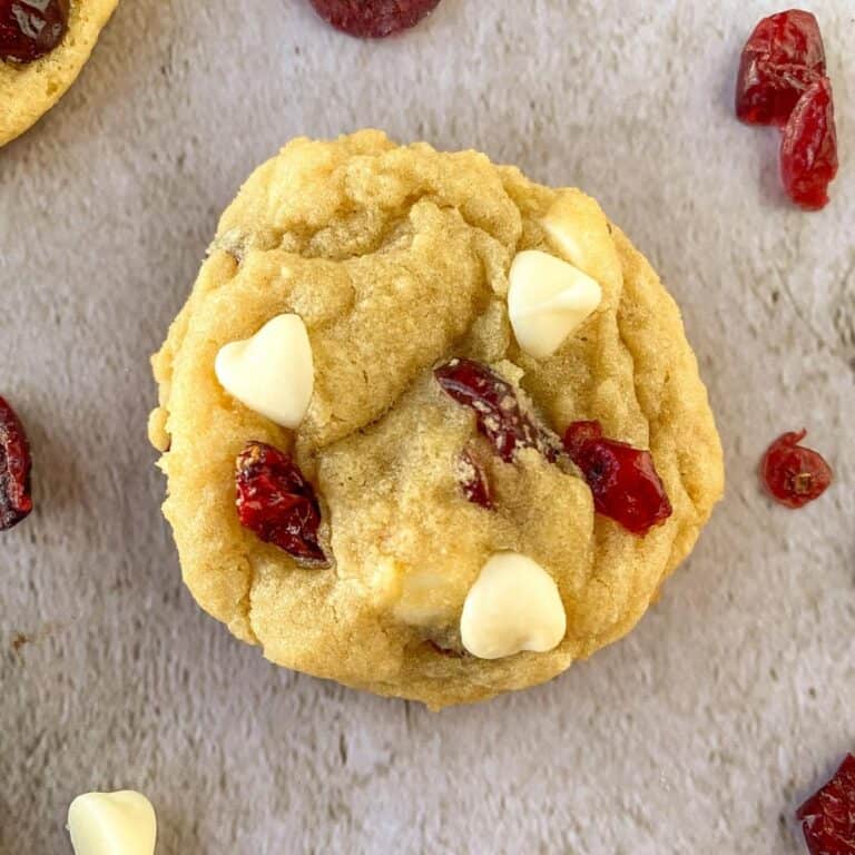 close up of white chocolate chip cranberry sugar cookie with cranberries and white chocolate chips scattered around
