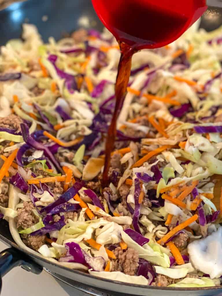 soy sauce being added to coleslaw and turkey mixture in a pan