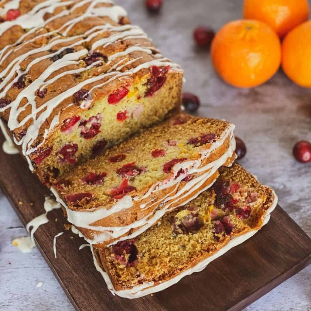 glazed cranberry orange quick bread sliced with oranges and cranberries in the background