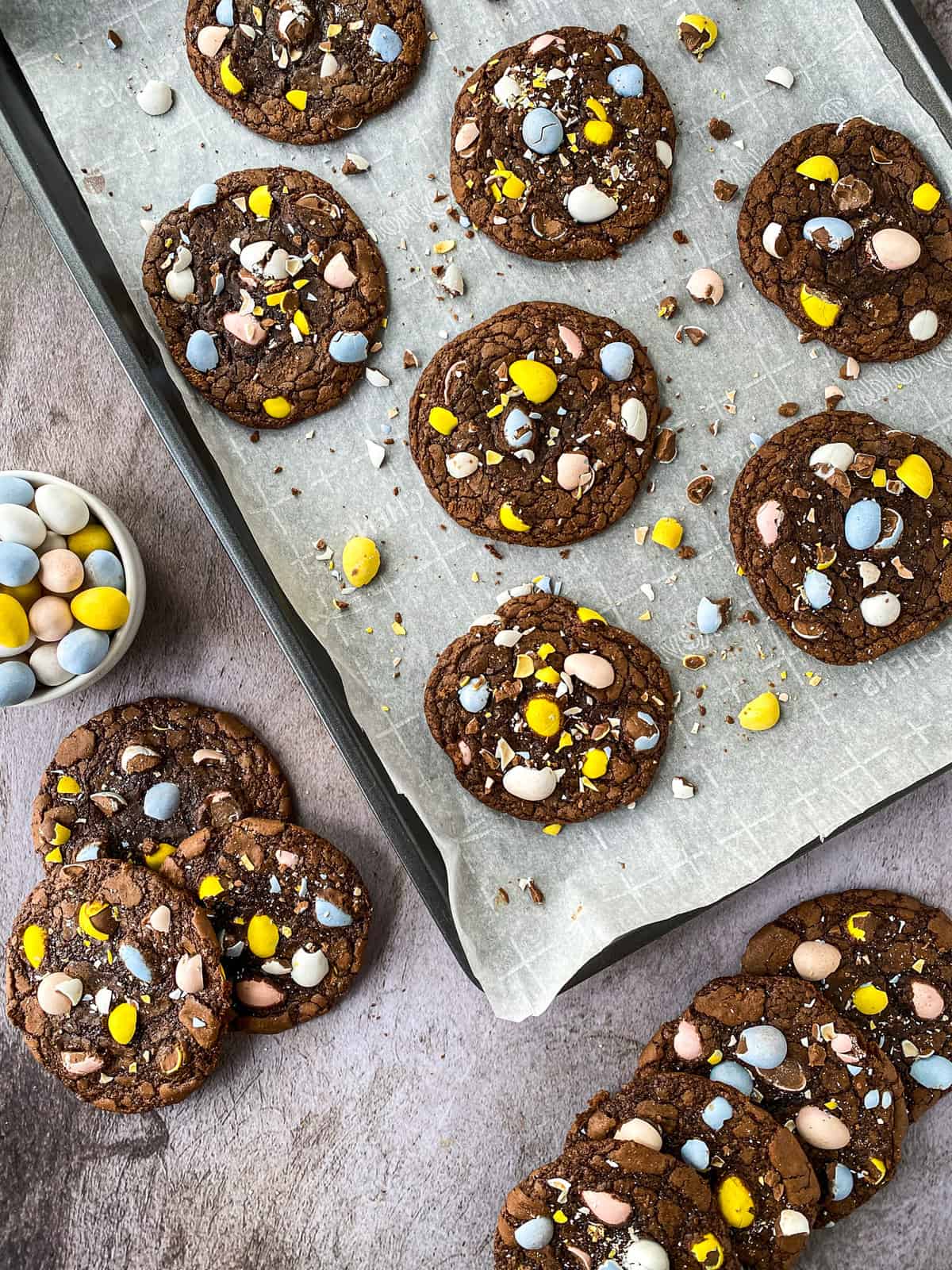 cookies on a table with a bowl of cadbury mini eggs and a baking sheet full of cookies
