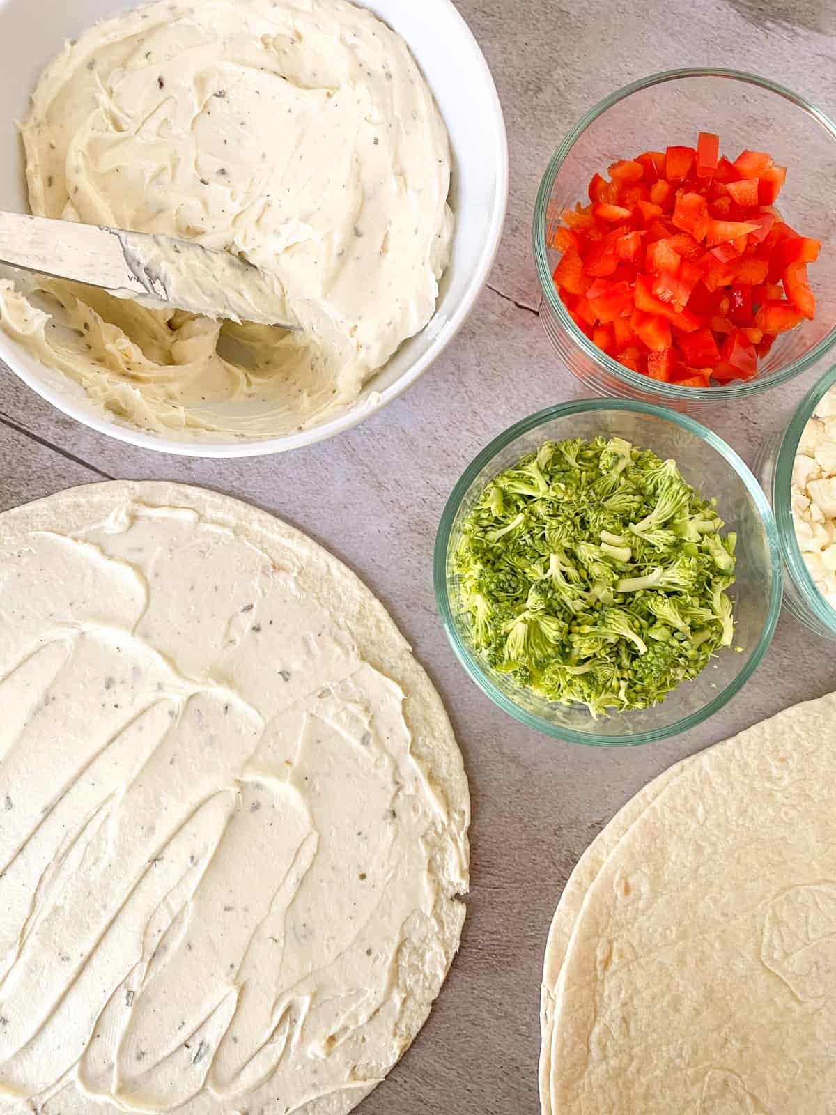 assembling the pinwheels with spread on a tortilla and the ingredients on the side