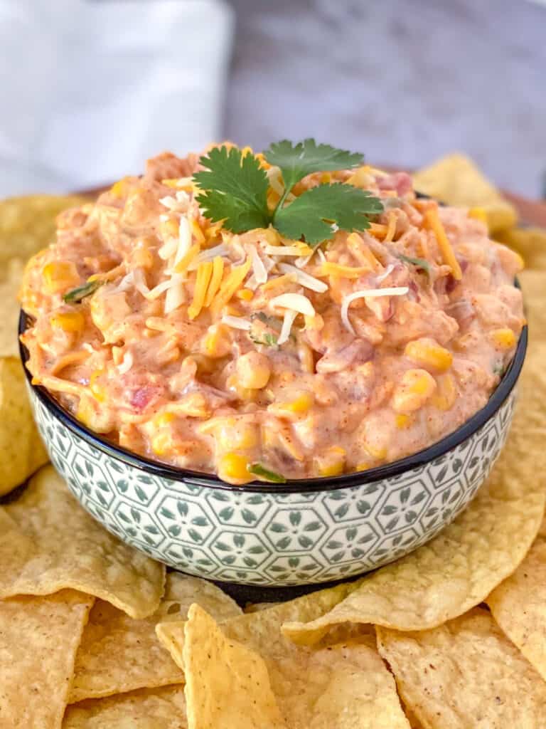 side view of corn dip in a bowl with cilantro on top surrounded by tortilla chips