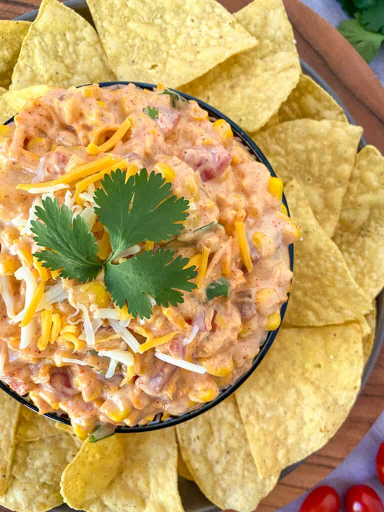 close up of corn dip in a bowl with cilantro on top surrounded by tortilla chips
