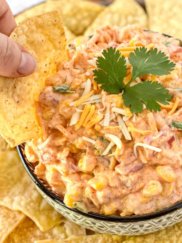 a hand scooping the corn dip in a bowl with a tortilla chip