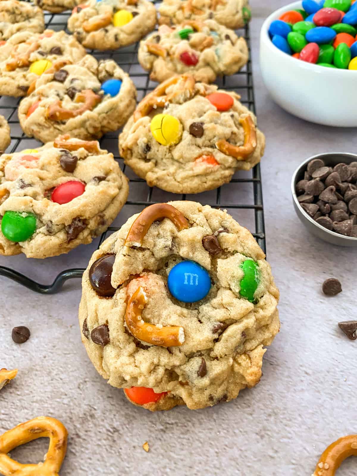 a cookie resting on a full cookie sheet with chocolate chips and a bowl of m&m's in the background