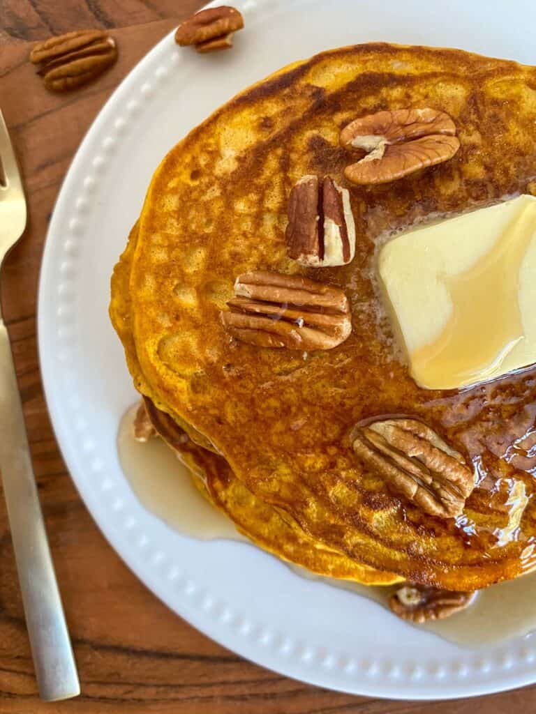 top view of a stack of pancakes with butter, syrup and pecans on top