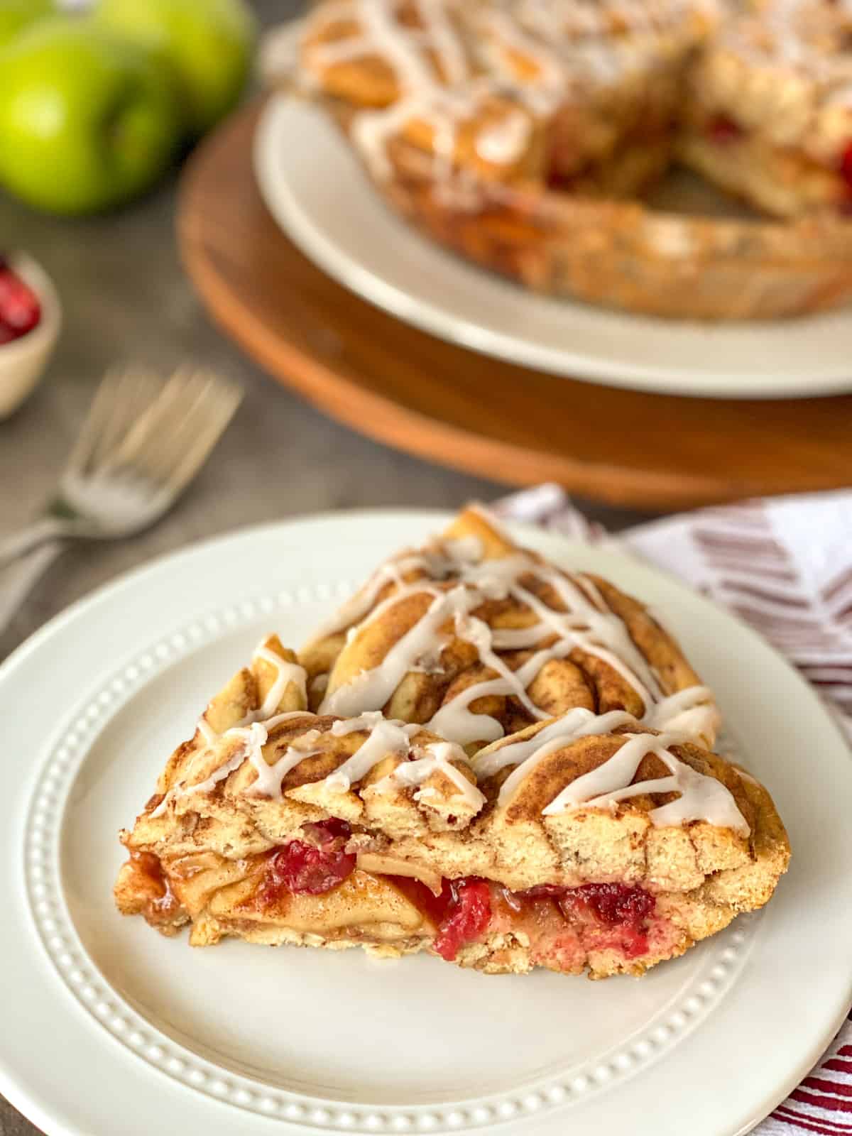 slice of cinnamon roll cranberry apple pie on a plate with a full pie without one slice in the background