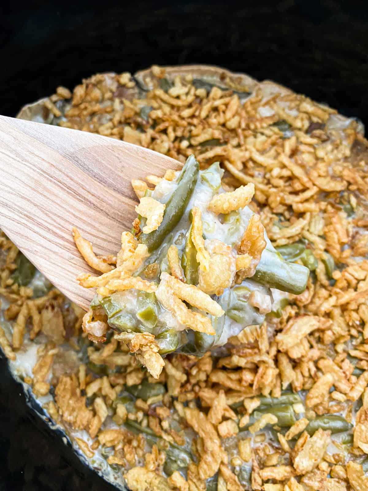 spoon full of classic slow cooker green bean casserole with a crock pot full in the background