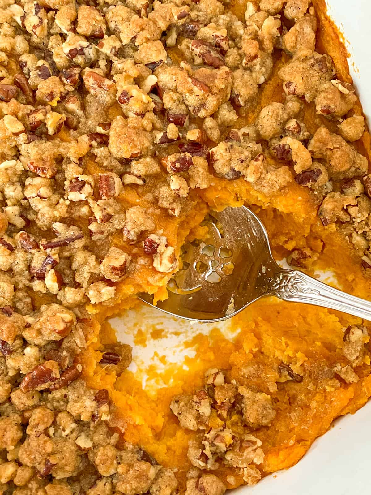pan of easy old fashioned sweet potato casserole with pecan topping and a spoon scooping it out