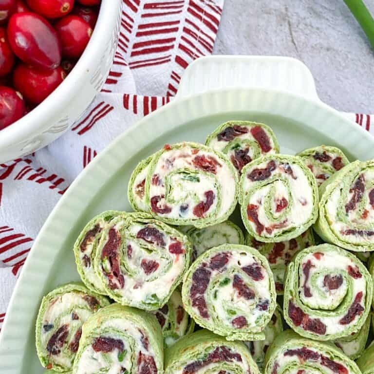 platter of cranberry feta pinwheels with cream cheese and a bowl of cranberries on the side