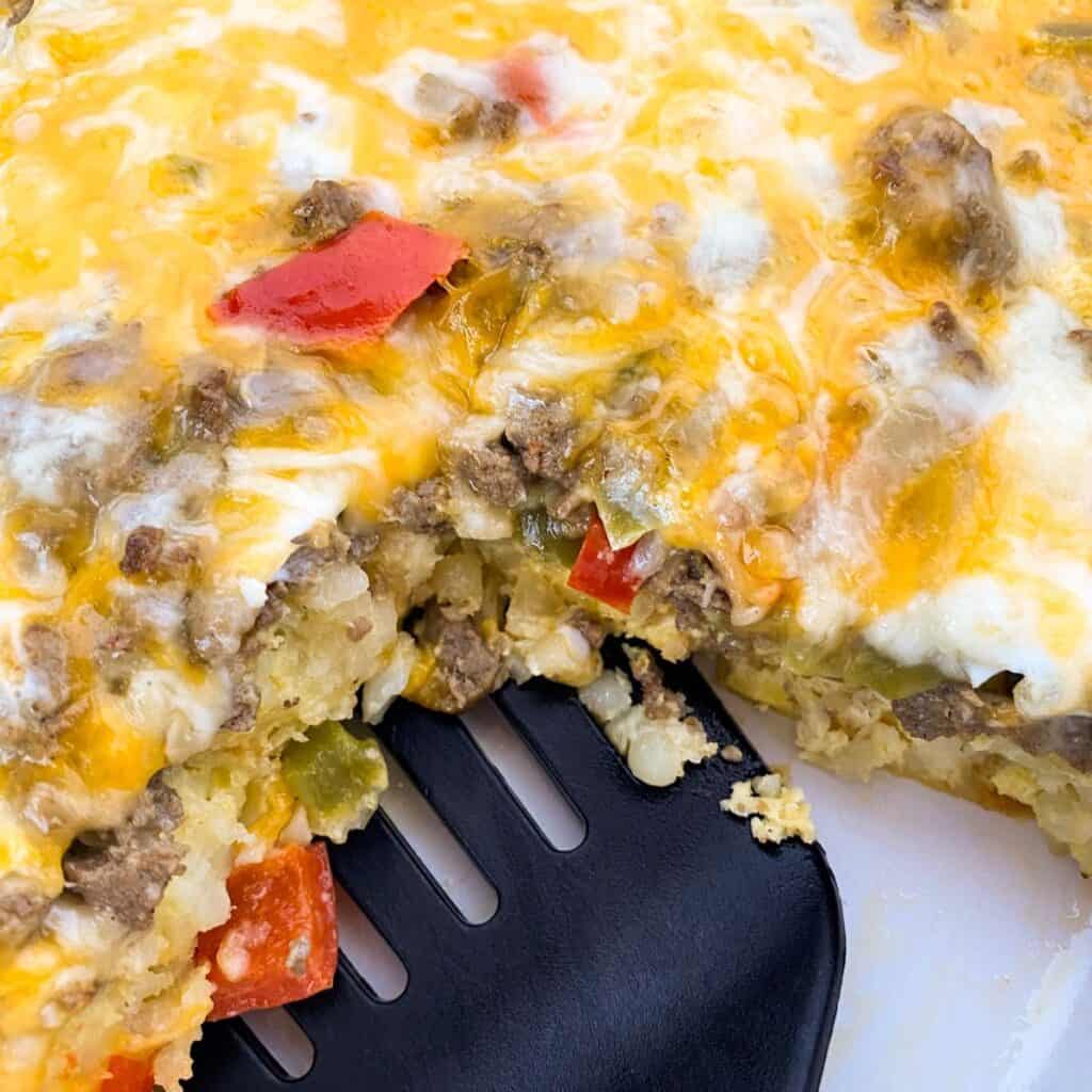 a spatula scooping out a piece of Overnight Tater Tot Breakfast Casserole (Make-Ahead)