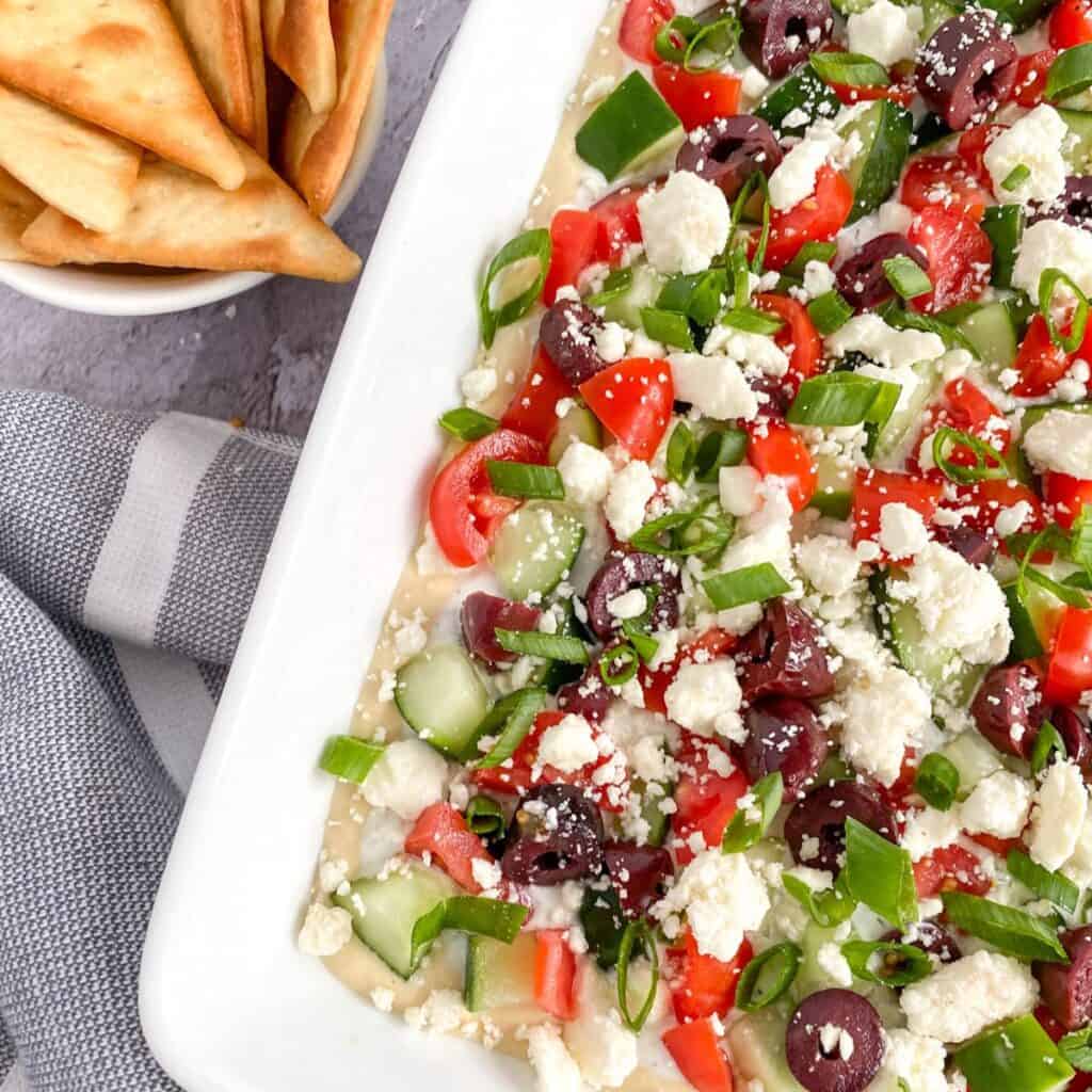 best greek 7 layer dip in a dish with pita chips on the side