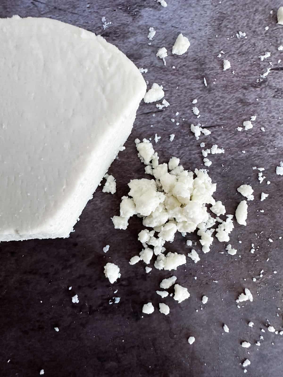 a block of cotija cheese with crumbled cheese on the table