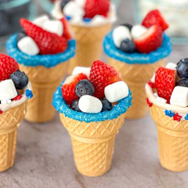 a group of patriotic fruit ice cream cones with blueberries strawberries and marshmallows on top