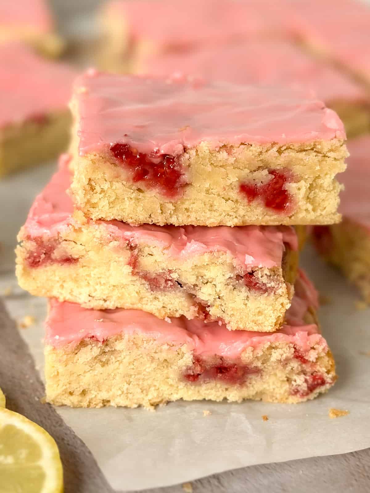 close up of a stack of 3 raspberry lemon blondies with more in the background plus lemons
