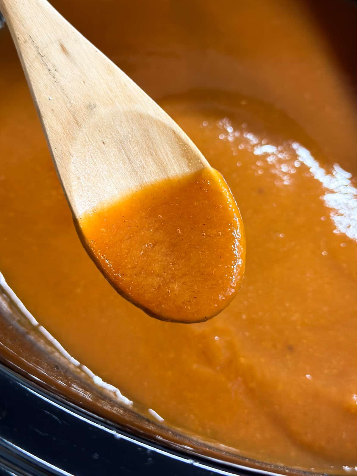 a large wooden spoon in a crock pot of peach butter