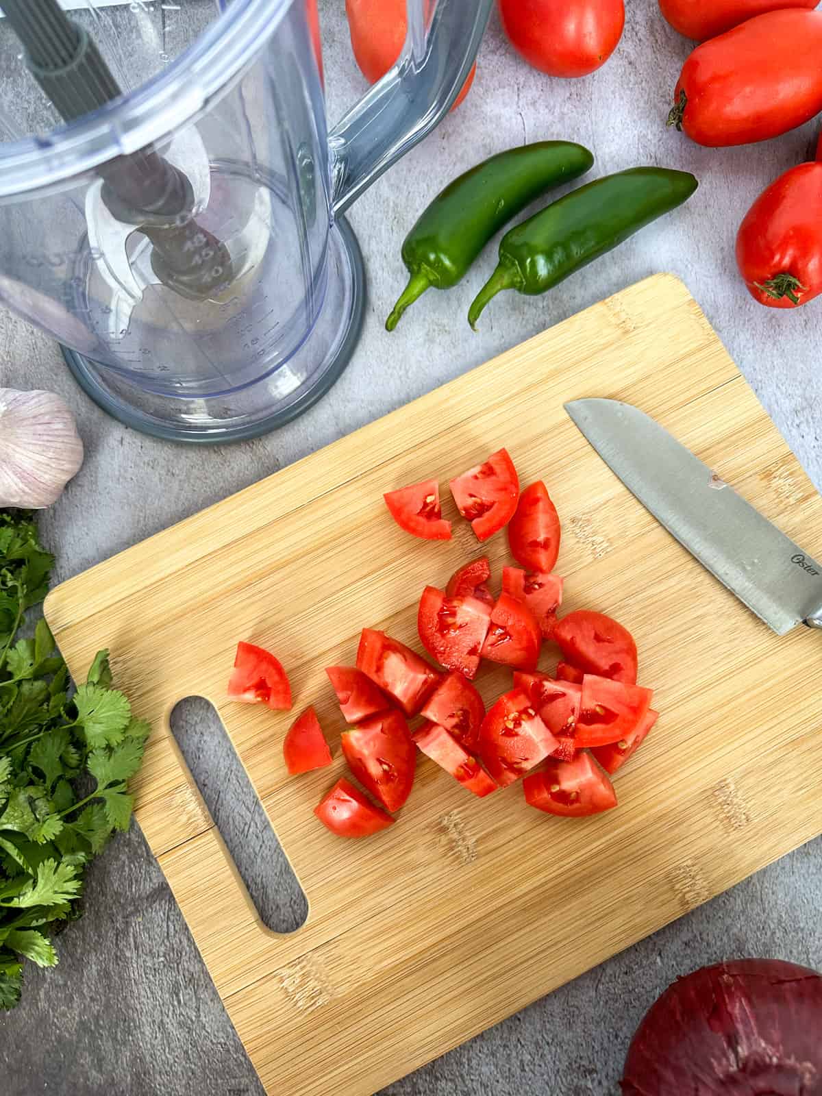 chopping tomatoes on a cutting board with cilantro, jalapenos, and garlic on the side
