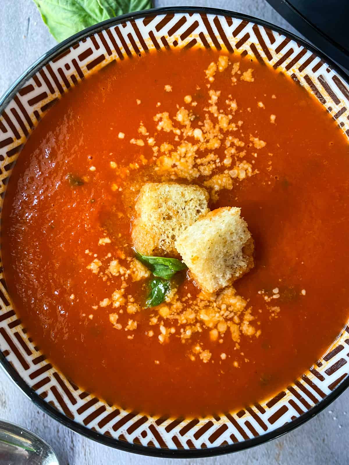 close up of easy slow cooker tomato basil soup in a bowl with croutons, basil leaves, and a sprinkle of parmesan cheese