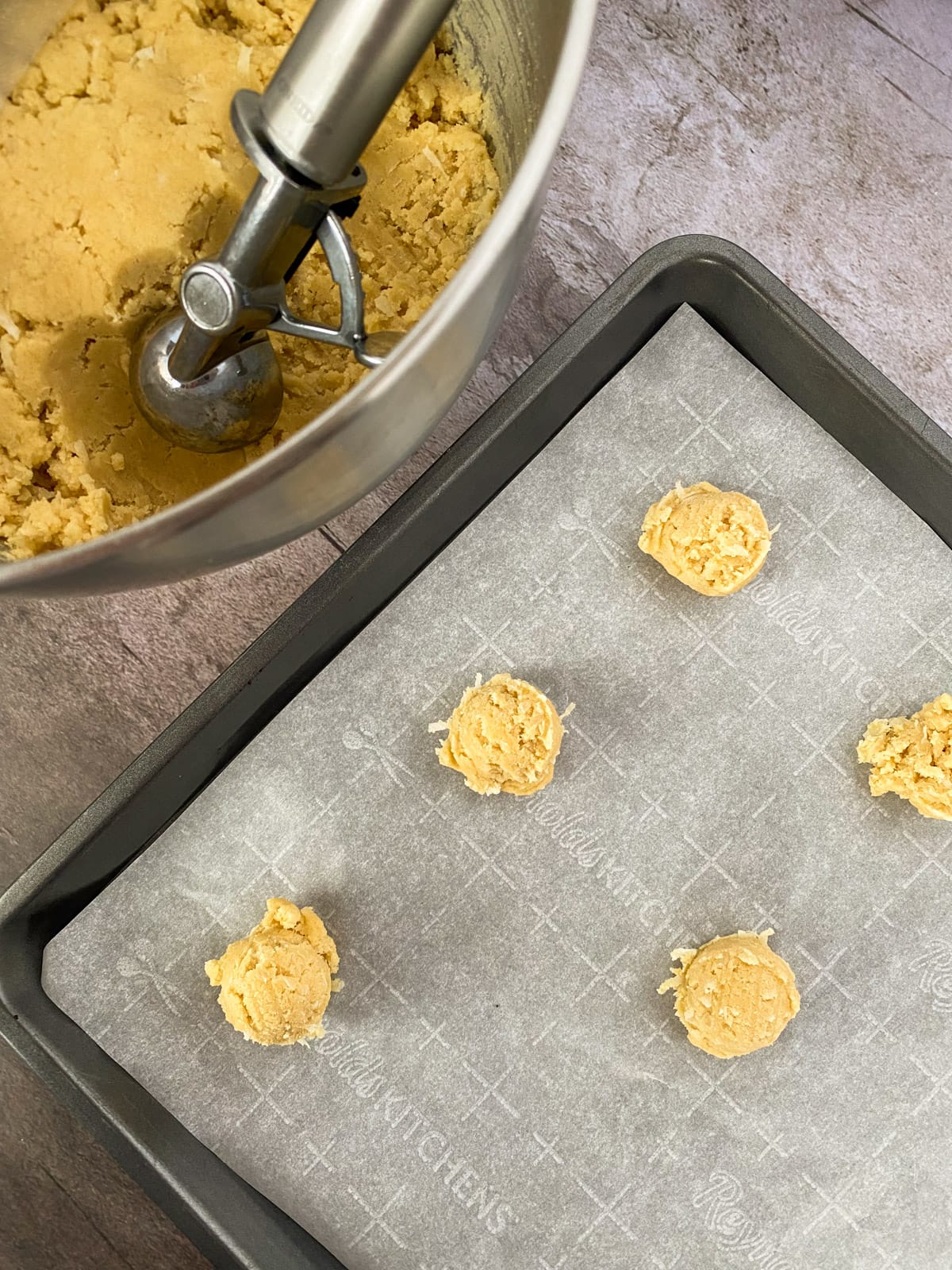 Scooping cookies from a mixing bowl onto a parchment paper lined baking sheet.