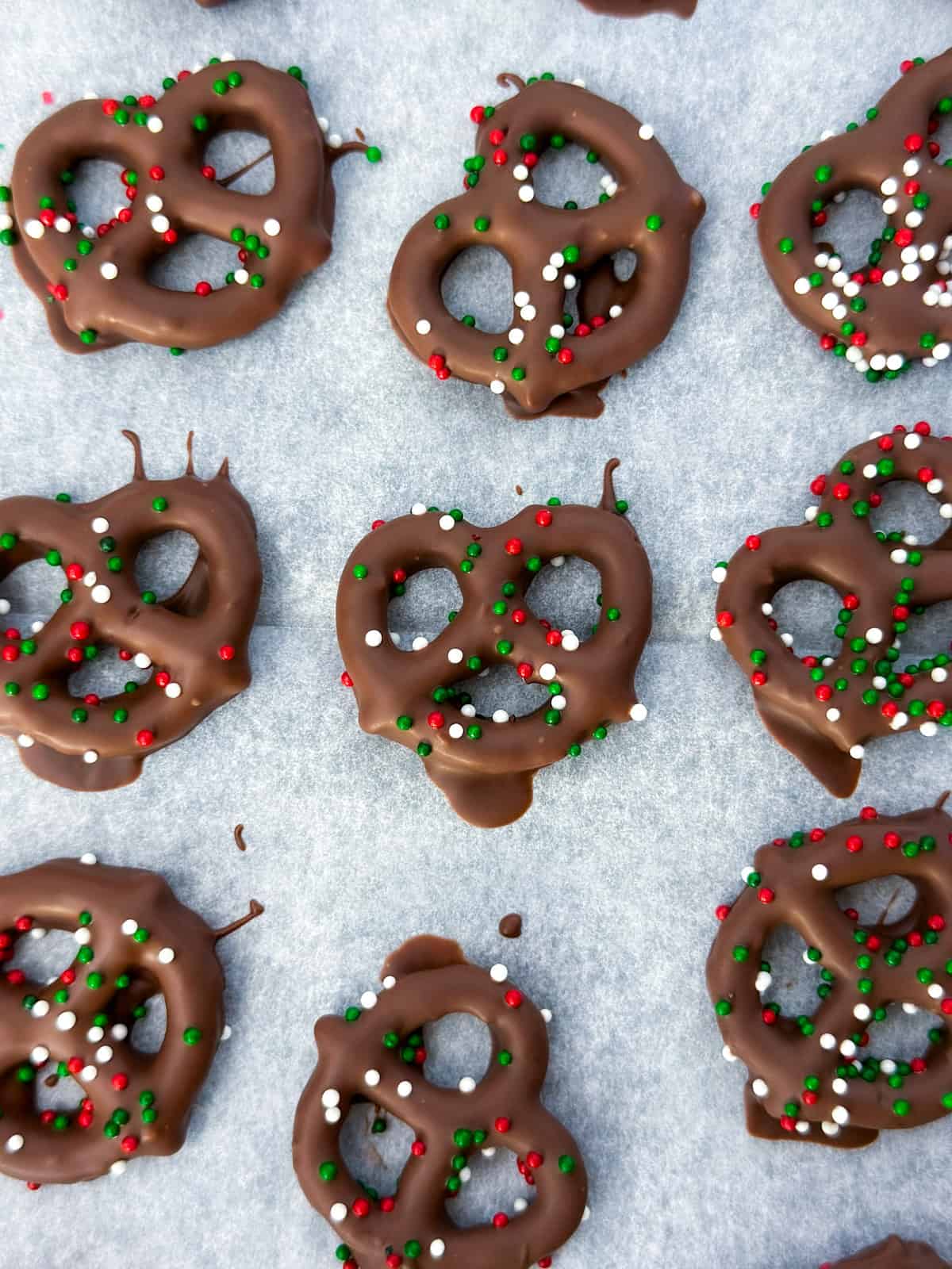 Chocolate covered pretzels with sprinkles on a piece of parchment paper.