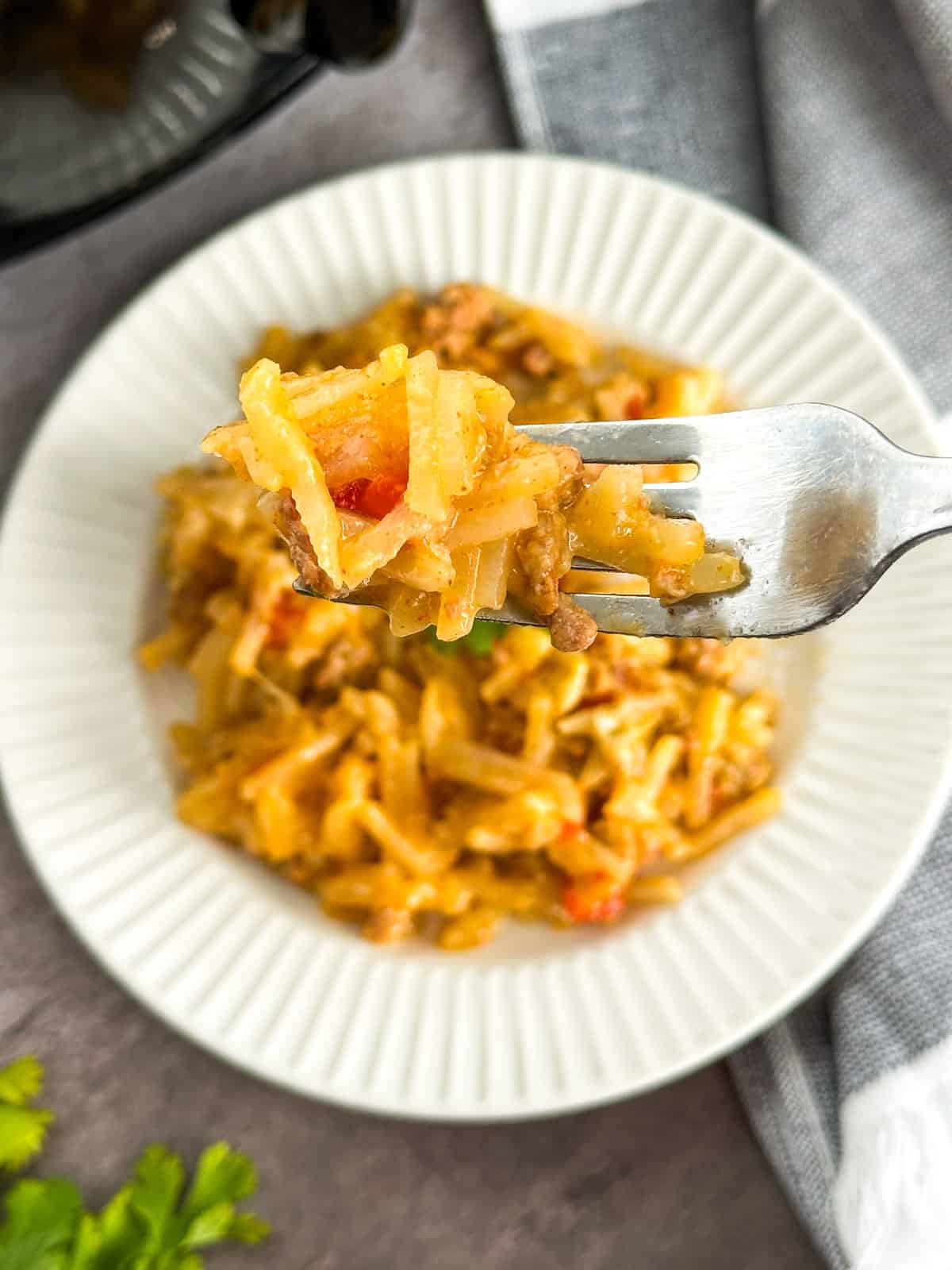 A fork scooping out the Taco Hash Brown Casserole from a plate.