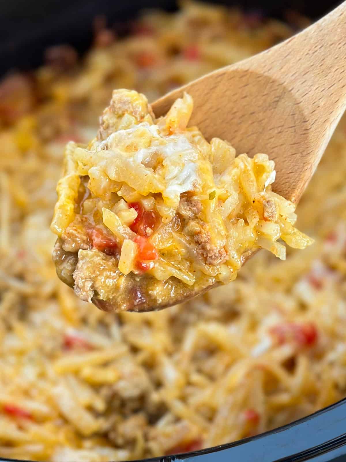 Crockpot Cheesy Taco Hash Brown Casserole scooped from a Crock Pot onto a wooden spoon.