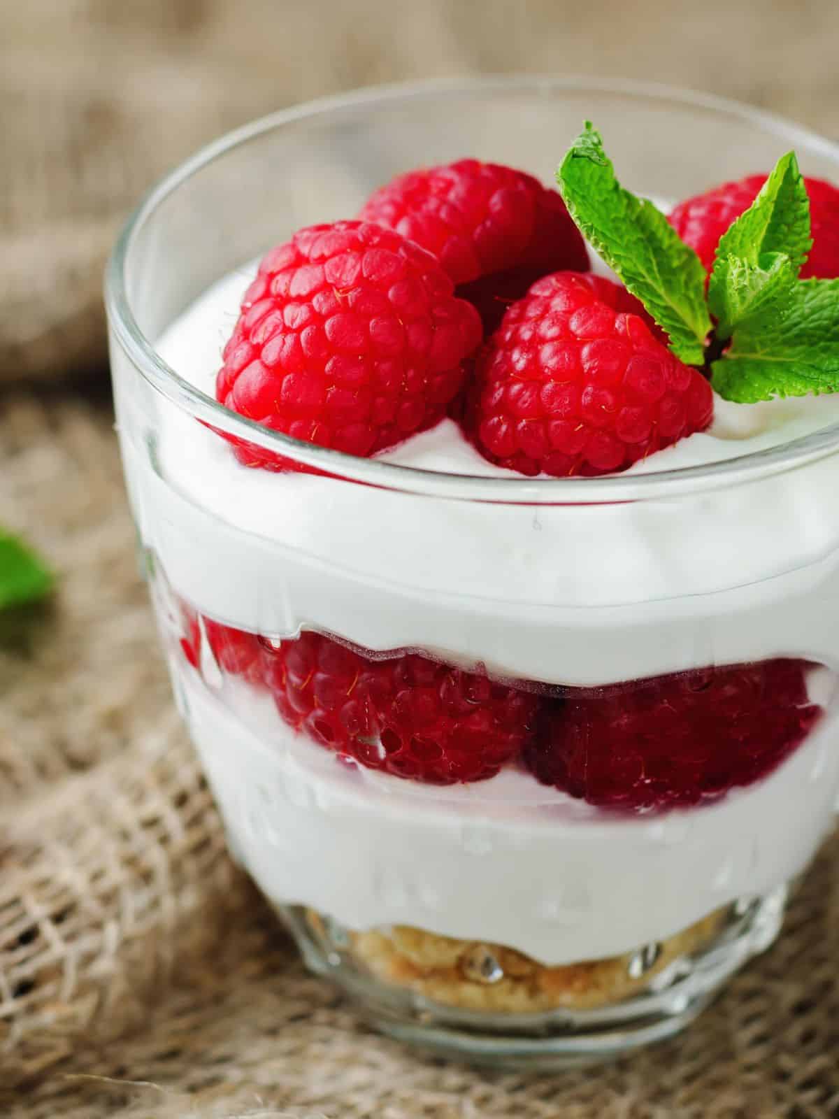Clear bowl layered with greek yogurt, raspberries, and granola then topped with fresh mint leaves.