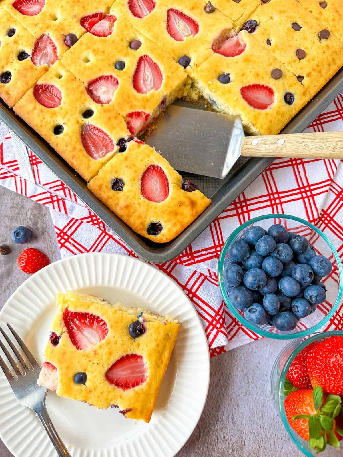 Sheet Pan Pancakes with one scooped on a plate with a bowl of strawberries and blueberries on the side.