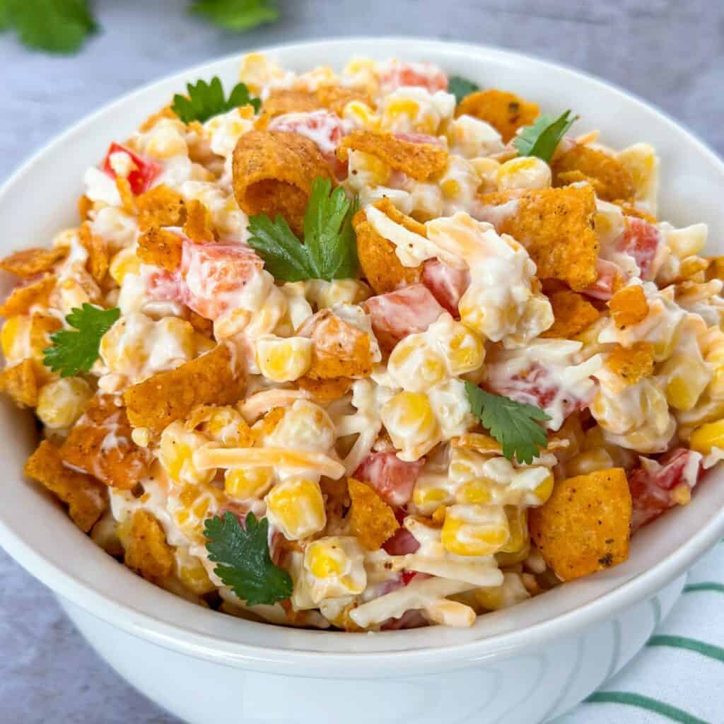 A bowl of Chili Cheese Fritos Corn Salad with cilantro on top.