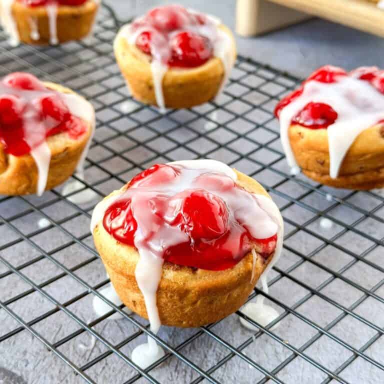 A cooling rack with cherry pie cups and icing drizzled over the top.