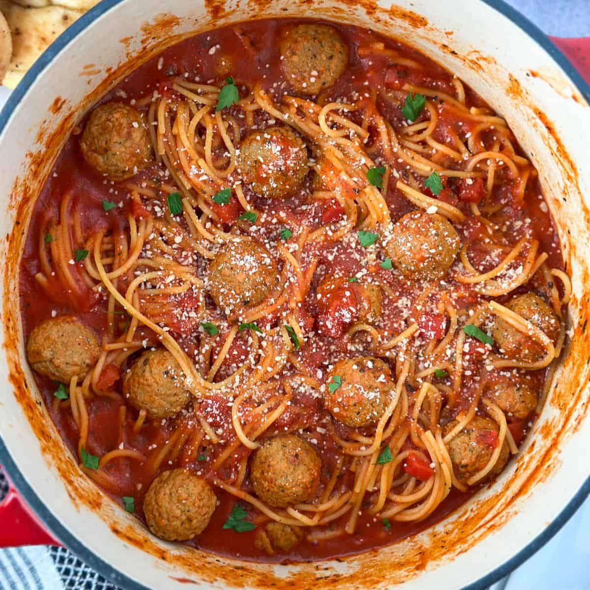 A pot with spaghetti and meatballs with a plate of garlic knots next to it.