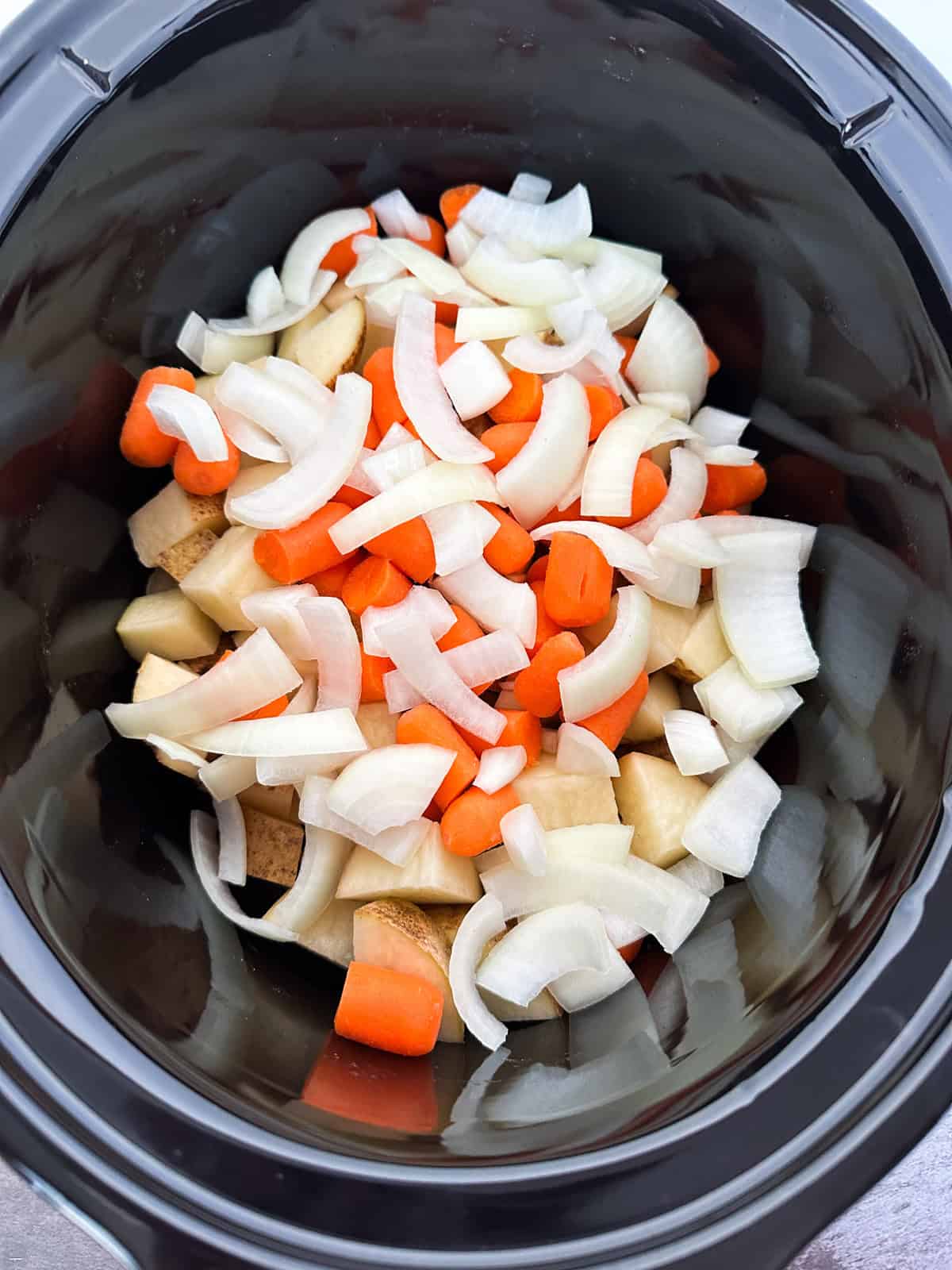 Potatoes, carrots, and onion in a crock pot.