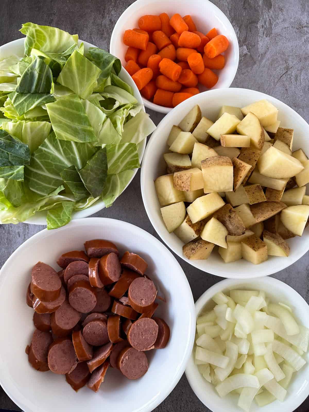 The ingredients for A crock pot filled with Sausage, Potato, and Cabbage on a table.