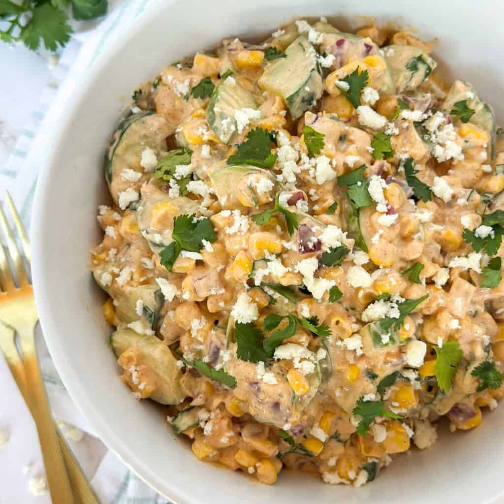Creamy Mexican Street Corn Cucumber Salad in a bowl with forks and cilantro next to it.