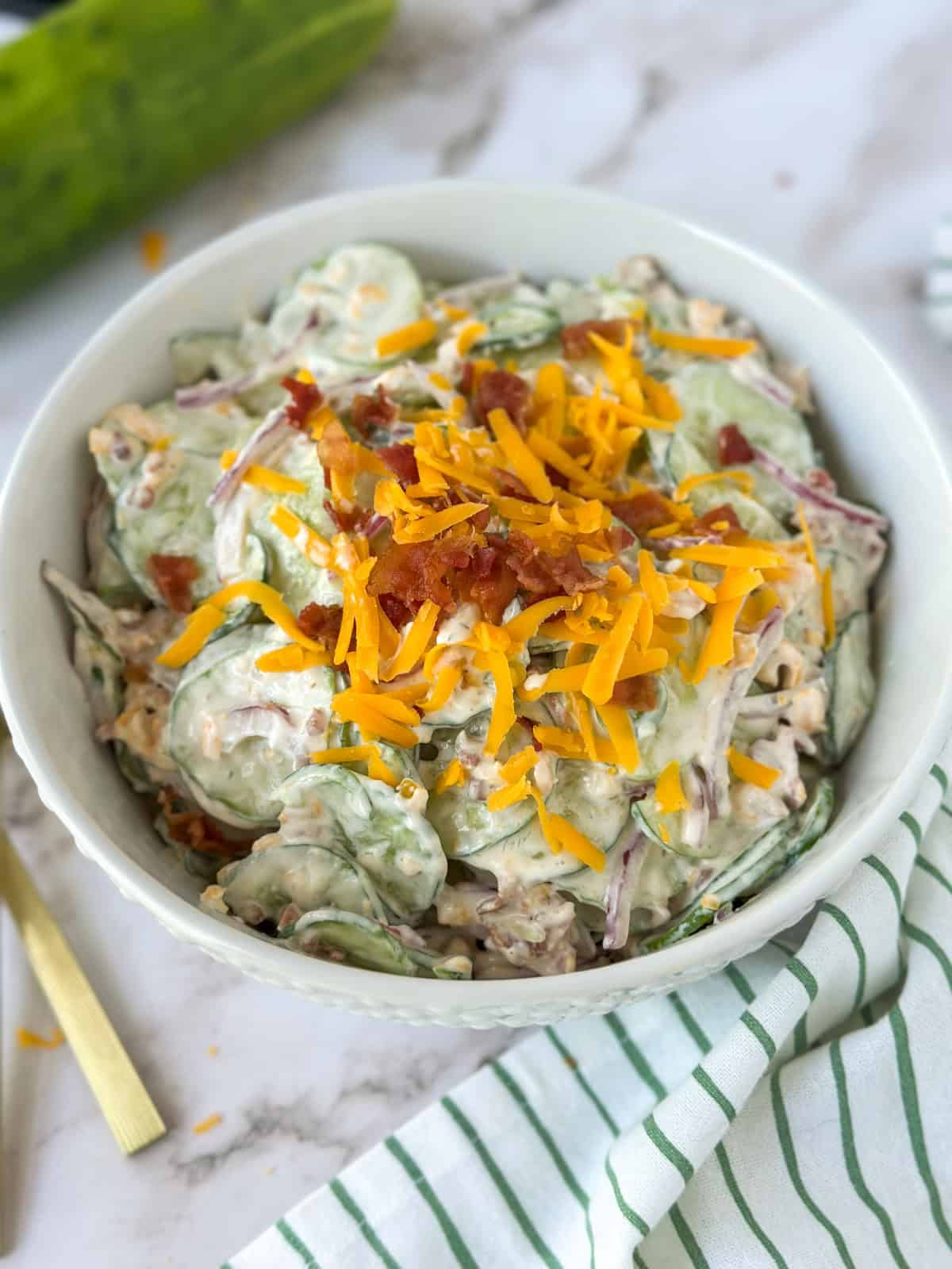 A bowl of Jalapeño Popper Cucumber and Onion Salad with extra cheese and bacon on top.