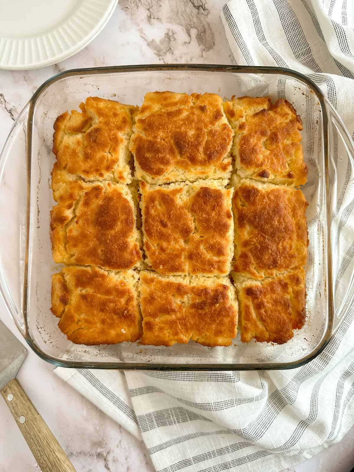 A pan of buttermilk butter swim biscuits with a cloth napkin, plate, and serving spatula.