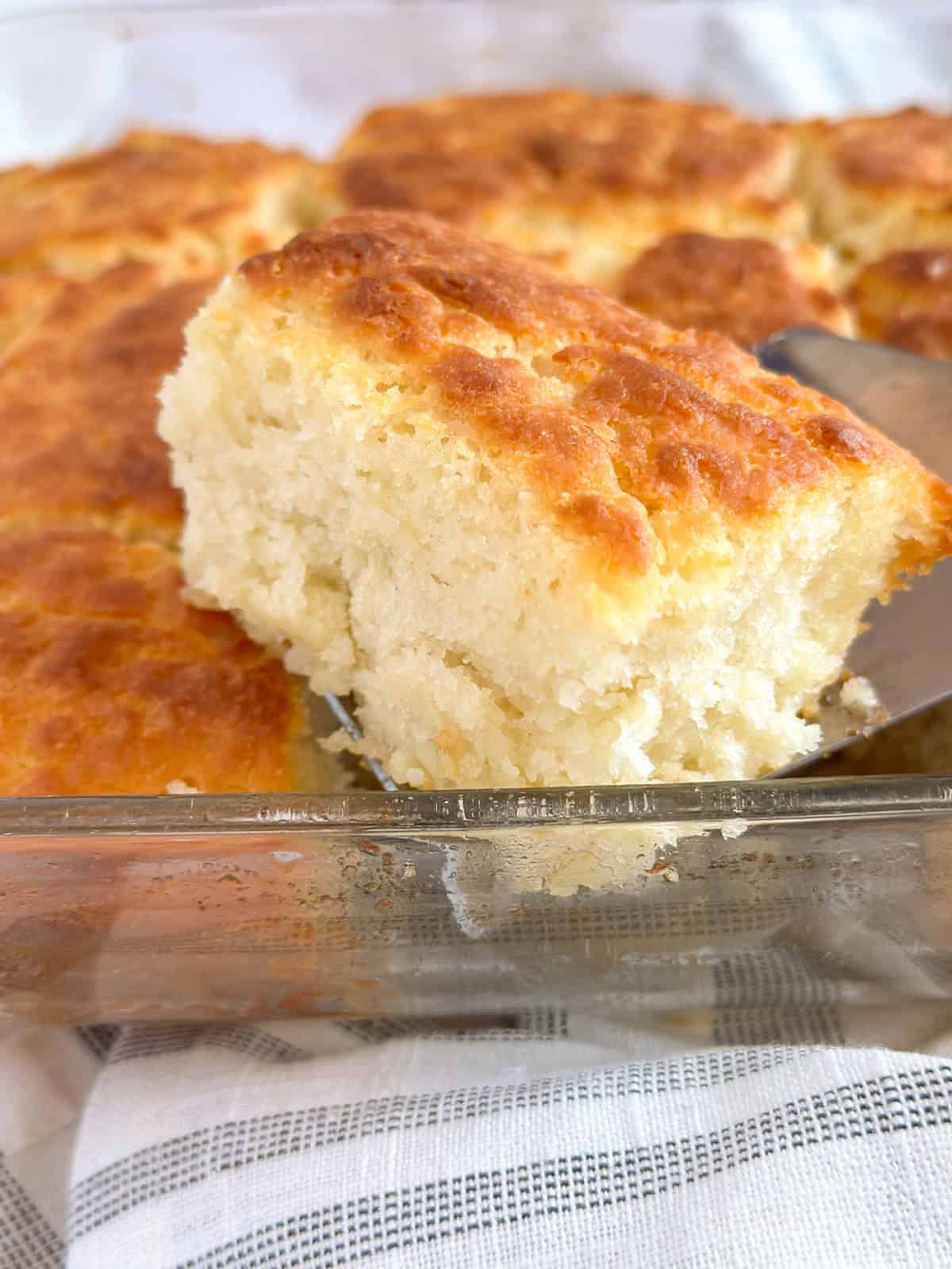 A slice of an Old-Fashioned Buttermilk Butter Swim Biscuit scooped on a spatula from a pan of biscuits.