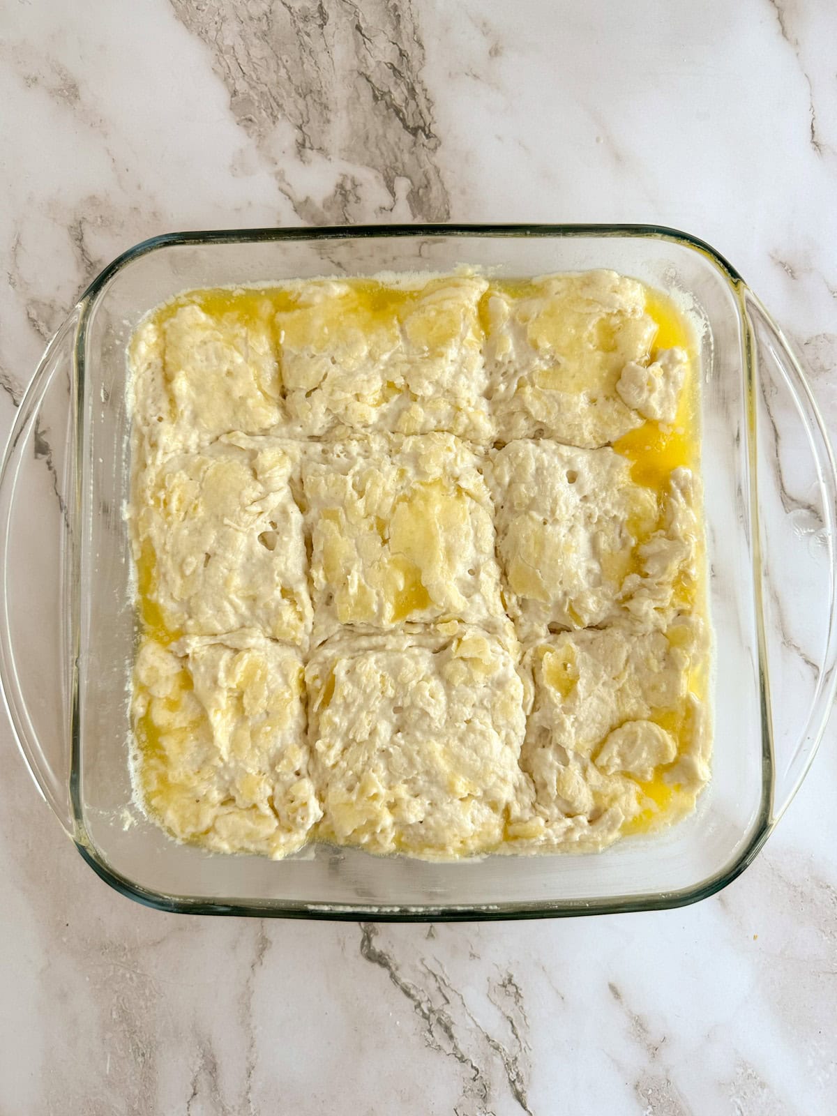 A pan of biscuit dough sliced into 9 slices before it is baked.